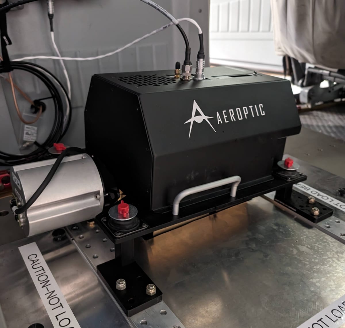 Aeroptic 40k RGB sensor, a black enclosure with the Aeroptic logo, mounted on its plate inside an aircraft