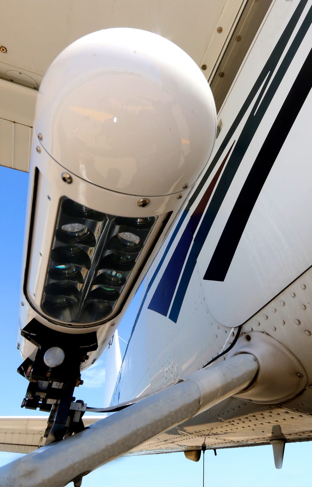 Close-up of an Aeroptic multispectral GeoPod mounted under a Cessna wing, showing its camera window